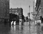 Residents attempting to keep their clothes dry as they cross at the intersection of Fourth and Nebraska streets during the Floyd River flood in 1953. Sioux City Museum