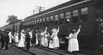 Raleigh American Red Cross canteen volunteers handing out pamphlets and other items to American troops leaning out of their train during a stop at the Johnston Street train station in Raleigh, circa 1918. Courtesy State Archives of North Carolina / #WWI 6.B3.F10.9
