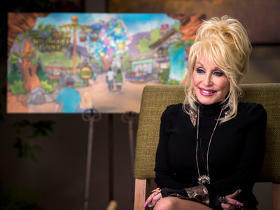 Dolly Parton seated in front of a Dollywood expansion rendering