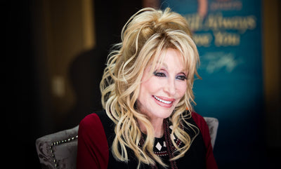 Dolly Parton smiling in front of an I Will Always Love You banner