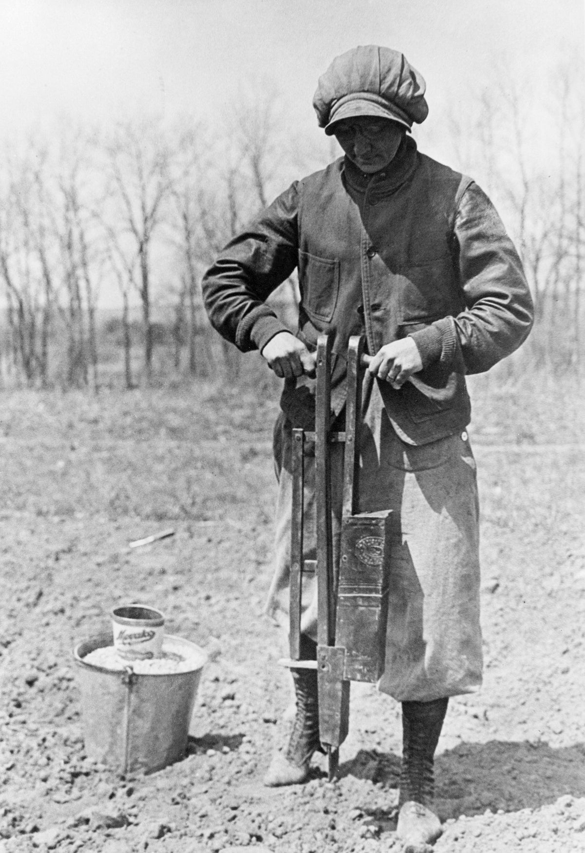 Nancy Hendrickson uses a planter to plant corn in a field, likely on her farm in Mandan. A bucket of seed is visible next to her. Courtesy State Historical Society of North Dakota / #00024-H-00045