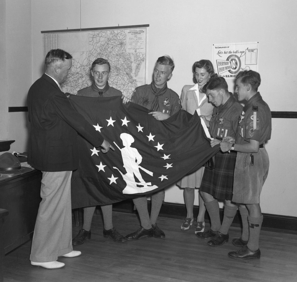 Two adults and four boy scouts view a World War II Minuteman US Treasury Savings Bond Company Enrollment Award Flag during a War Bond Rally in Fredericksburg in 1942. Courtesy Library of Virginia, Chamber of Commerce Collection