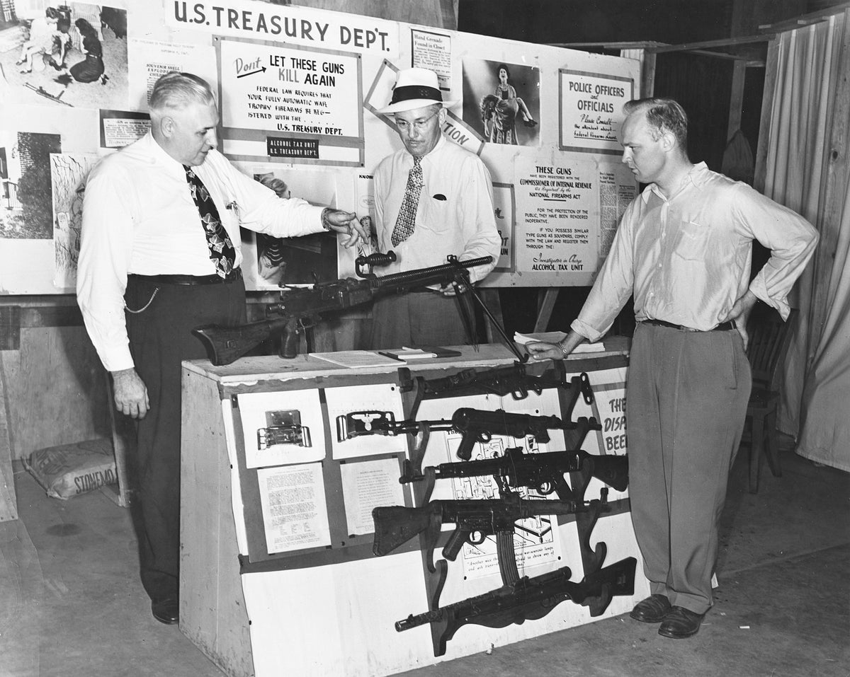 Pointing to lethal features of a Japanese-made machine gun on exhibit with many other automatic weapons in the Illinois State Fair grandstand, are James B. Cornet, left, and Lloyd R. Doyle, treasury department agent from East St. Louis. Intent observer is Walter Jackson, of Springfield, standing right, circa 1945.