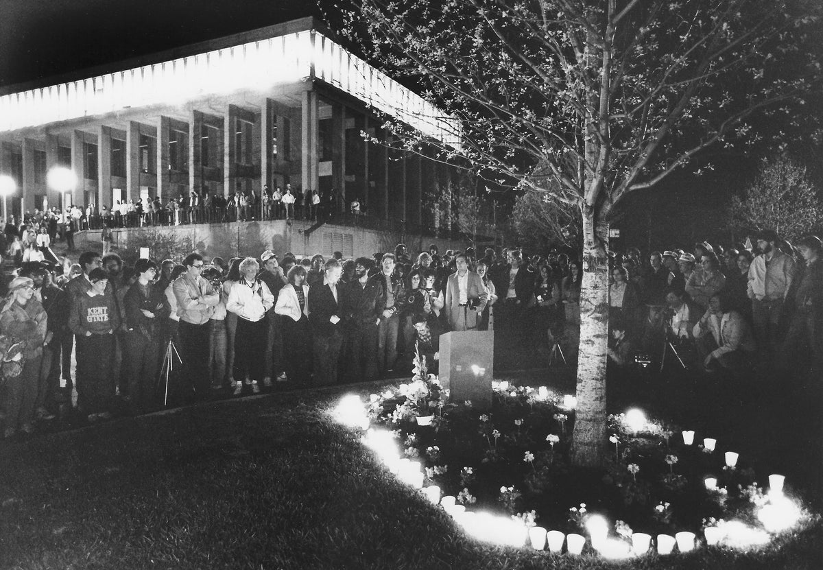 A crowd gathers on the edge of the Prentice Hall parking lot during the annual May 4 candlelight vigil observance at Kent State on May 3, 1982. The candles surround the small memorial at the edge of the parking lot — Taylor Hall is in the background. Courtesy Akron Beacon Journal