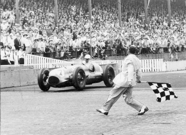 Waving his hand in a victory salute, Bill Holland flashes across the finish line in his Blue Crown Special. Holland set a race record by averaging 121.327 mph for the 500 miles. Signaling the victory with the traditional checkered flag is Bill Vanderwater, assistant chief starter. Star file photo