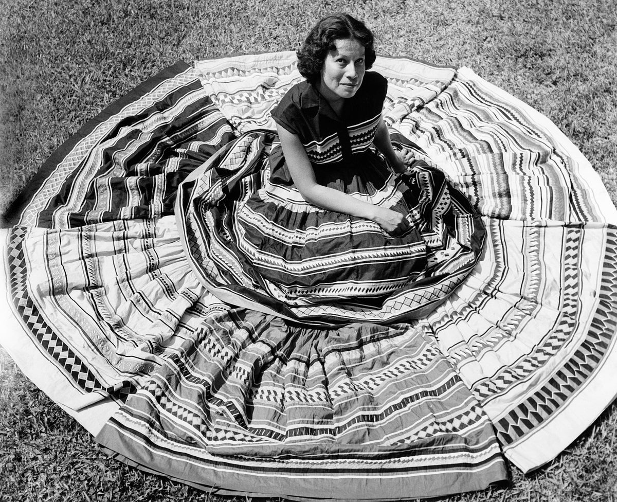 Agnes Johns (Bird Clan) posing for a crafts advertisement with a display of 10 patchwork skirts made by Seminole women for the Seminole Arts and Crafts Guild, circa 1955. Courtesy The Seminole/Miccosukee Archive