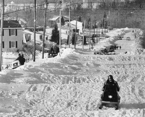 A snowmobiler travels up Rogers Road, still closed on the afternoon of February 2 with 10-12 foot deep snow spanning the width of approximately 1/2 mile of the road. Snowmobiles were the key transportation link, carrying food and medicine and ferrying police and doctors through clogged streets. Courtesy Dennis C. Enser/Buffalo News
