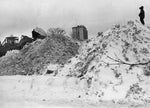 A figure at right watches as piles of snow are moved. Courtesy Ron Moscati photo, The Courier-Express Photograph Collection. Archives & Special Collections Department, E. H. Butler Library, SUNY Buffalo State