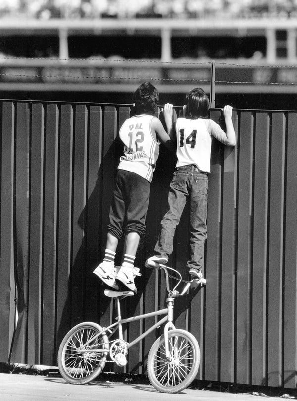 Two kids watch the game action over the fence outside the southwest corner of Mile High Stadium, Oct. 5, 1987. On the left is Jose Baeza, age 12, on the right, John Gonzales, age 13. The Denver Post