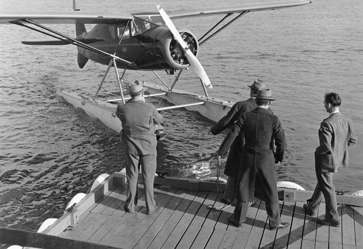 A high-wing, single-engine airplane with pontoons arrives at dock, circa 1940. Four men stand on the dock, ready to help secure the plane. Courtesy Indian River County Historical Society Collection, Archive Center, Indian River County Main Library