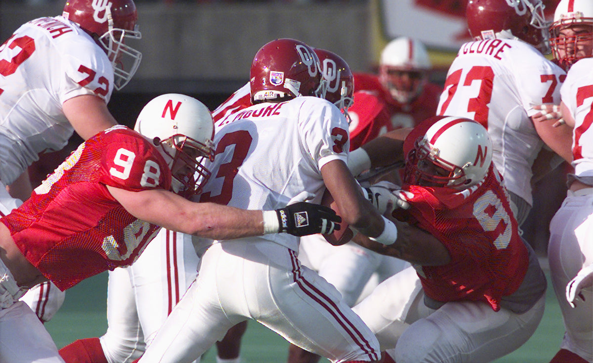 Grant Wistrom (98) and Steve Warren (96) force Oklahoma quarterback Eric Moore (3) to fumble in the first quarter. Wistrom had 10 tackles, two sacks and forced three fumbles. Courtesy Lincoln Journal Star