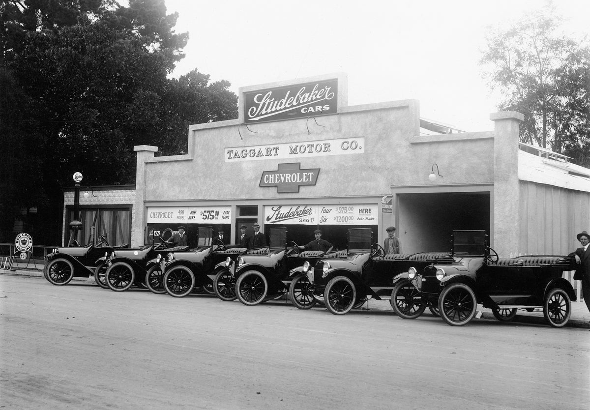 New cars parked in front of Taggart Motor Company, a Studebaker and Chevrolet dealership at 306–308 North Los Angeles Street, Anaheim, circa 1917. From left: unidentified (salesman), Fred Schroeder (salesman), John Taggart (co-owner), Paul Taggart (co-owner), Vincent “Dick” Bruce (mechanic), Dan Clemmer (mechanic), Bill Hauser (salesman). The Taggart building became the Quast Plumbing Service in the 1970s. Courtesy Anaheim Public Library