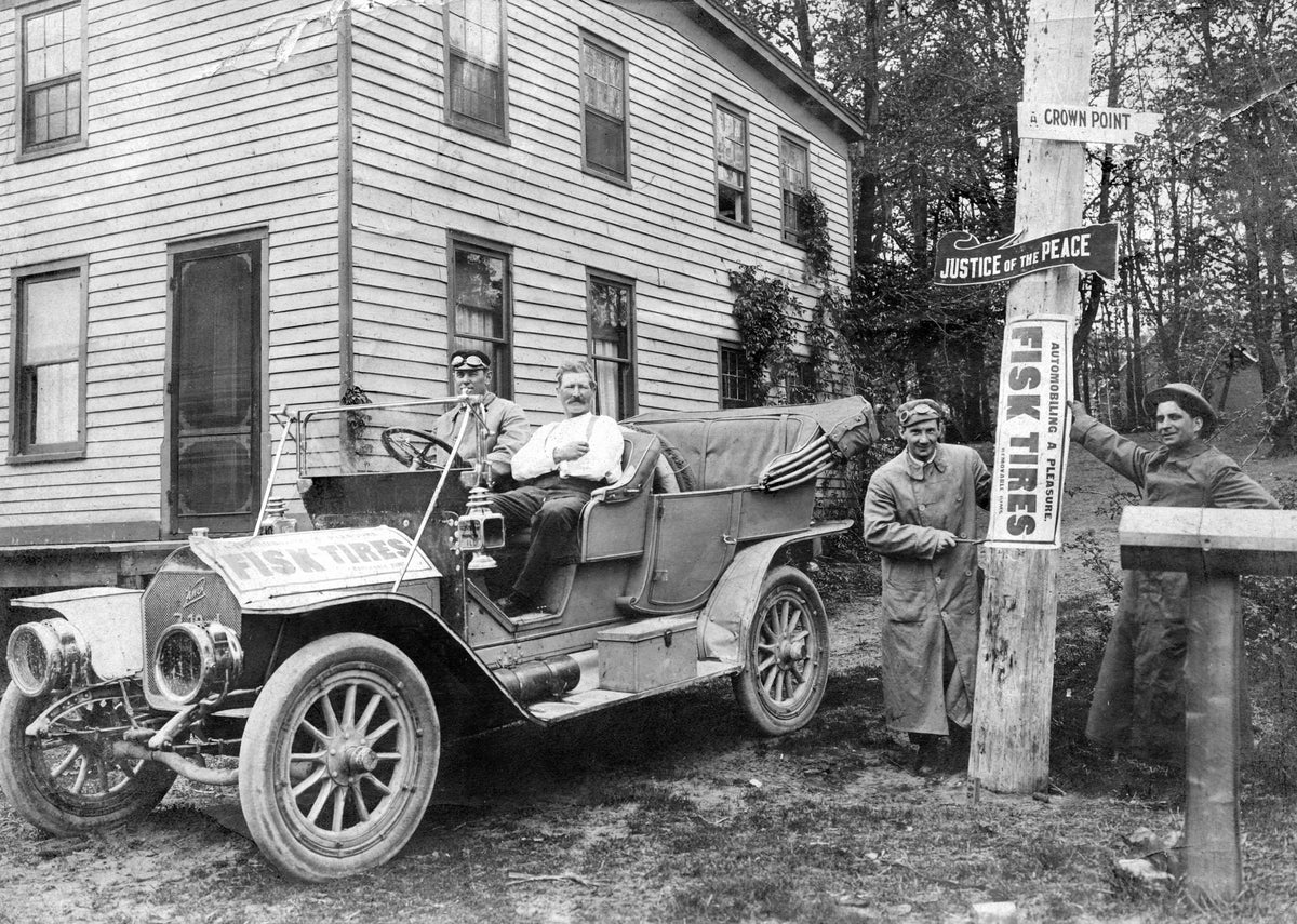 Hugo Kaske (passenger seat) gets a ride in an automobile advertising Fisk Tires in front of his home, originally the Brass Tavern and Inn built in 1845, on the corner of Ridge Road and Columbia Avenue in Munster, 1906. Courtesy Munster Historical Society
