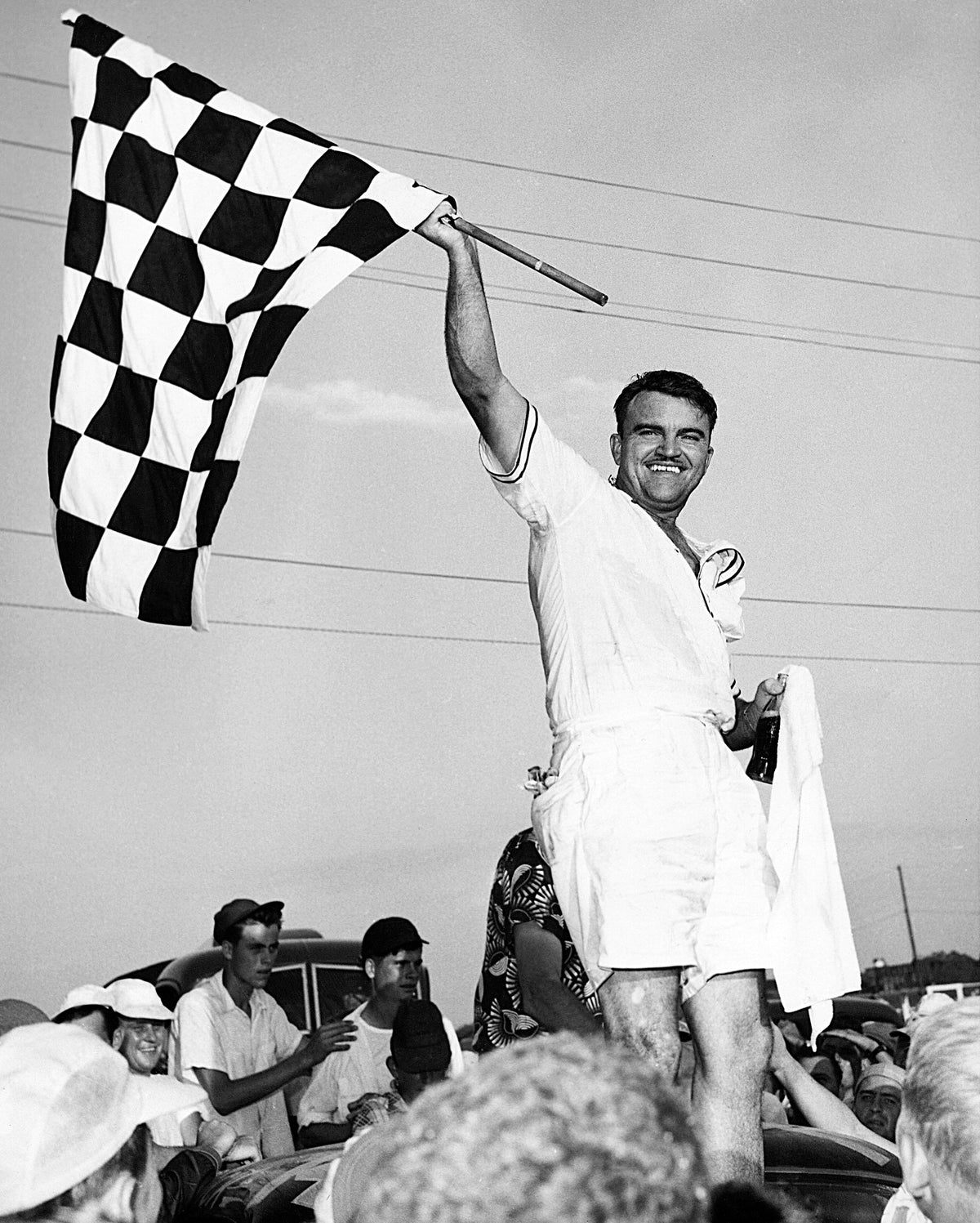Fonty Flock, wearing Bermuda shorts and a short-sleeve shirt, waves the checkered flag in 1952 after winning the third annual Southern 500 at Darlington Raceway. CourtesyISC Images & Archives Via Getty Images