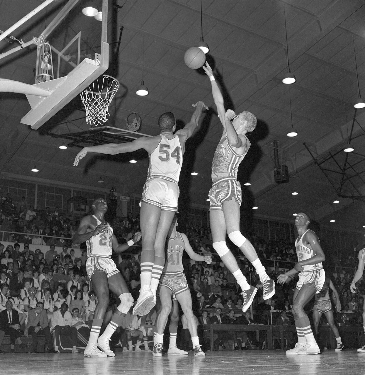 Basketball game between North Texas State University and Oklahoma City University, late 1960s. Willie Davis (54) is jumping to block a shot, while teammates Hamp Hazelton (22) and Matthew Huff (32) watch from the ground. Courtesy University Photography Collection (U0458), University of North Texas Special Collections / #UNTA_U0458-105-402-05