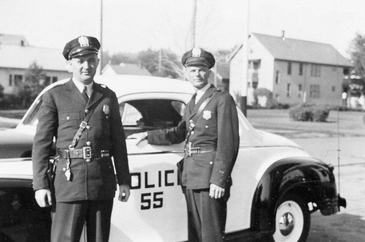 Police officer Henry Looft, right, and his partner (possibly Dave), at the Shell gas station on James Street at the corner of St. Vincent Street in Utica, 1941. In the background is the former James Street bus loop.