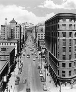 Elevated view of Seventeenth Street including the Brown Palace Hotel (right) and the Rocky Mountains in the distance, 1941. Note the mountains are in the wrong location in this photo; this image was altered and used for a postcard to attract tourists. Courtesy Denver Public Library, Western History Collection, #X-23414