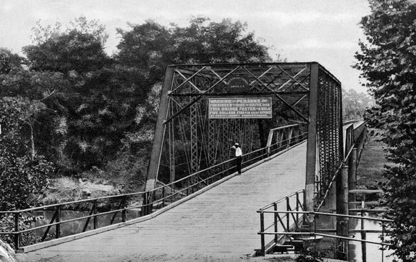 A man looks over the Tar River from the bridge in Greenville, circa 1912. The sign on the bridge reads: “Warning! All persons are forbidden to ride or drive over this bridge faster than a walk — Five dollars fine for every offence — By order of County Commissioners.” Courtesy East Carolina University Special Collections / #0441-s1-b1-fb-i5
