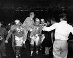 Detroit Lions celebrating on the field at Briggs Stadium after winning the 1953 NFL Championship. Joe Schmidt (#53) and Dick Stanfel (#63) hold coach Buddy Parker. Behind them stands Yale Lary (#28).Courtesy Detroit Historical Society / #2014.003.182