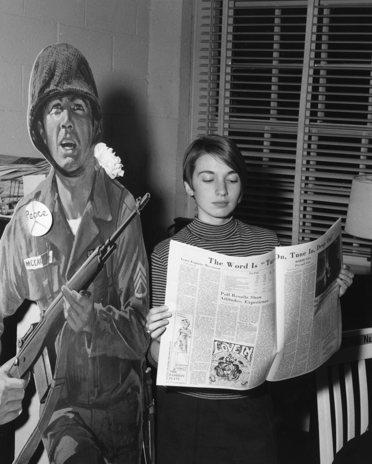 Mary Washington College student Liz Vantrease reads a copy of the student newspaper, The Bullet, next to a cut out of a Vietnam War soldier wearing a peace sign and flower, Fredericksburg, 1968. Courtesy University of Mary Washington, Special Collections & University Archives.