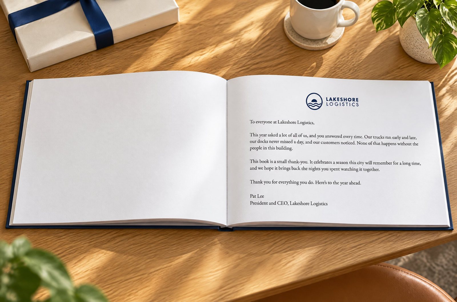 An open landscape hardcover on a light-oak desk. The right-hand page is a letter from Lakeshore Logistics’ CEO to employees, with the company logo at the top; the left-hand page is a plain white endpaper.